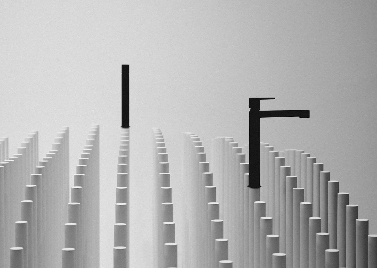 Sculptural black-and-white composition of a matte black faucet fixture among rows of pale columns