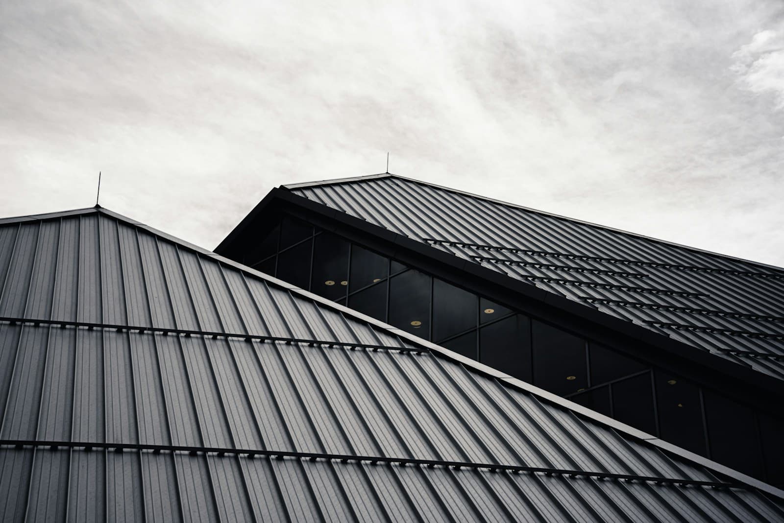 Dramatic low-angle photograph of a dark standing-seam metal roofline against a cloudy sky
